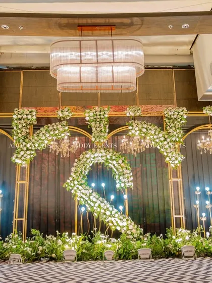 A direct, symmetrical view of the floral "S" stage design. This shot highlights the balance and precision in our decor, with chandeliers and lighting perfectly framing the central motif under a grand ballroom chandelier.
