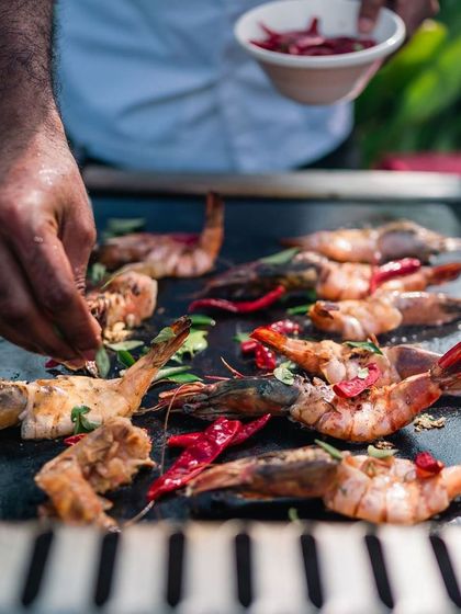 A chef seasons fresh prawns on a grill, a glimpse into the live cooking action that makes our brunches so special.