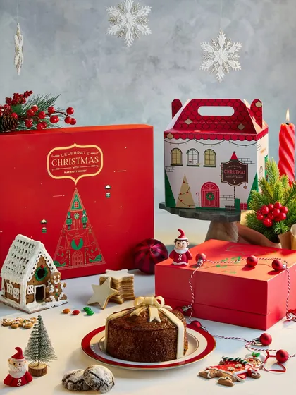 A full display of the Marriott Bonvoy Christmas hamper collection. This shot brings together the gingerbread house, cakes, and cookies into one abundant and festive scene, perfect for showcasing the entire range.