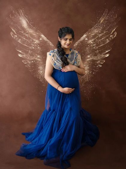 A whimsical portrait featuring a mom-to-be in a blue gown with sparkling angel wings edited in, creating a truly angelic look.