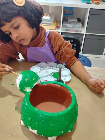 A toddler enjoying the sensory experience of painting a large turtle planter. Art is for all ages!