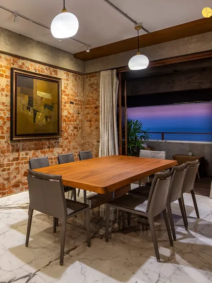 The dining room at 'The Canvas' at dusk. The space is designed to be a backdrop for the client's art collection and the stunning sea view, with exposed brick walls and marble flooring creating a play of raw and refined textures.