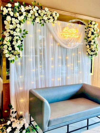 The same elegant white floral backdrop, this time paired with a modern grey loveseat. This shows how the backdrop can be customized with different seating options.