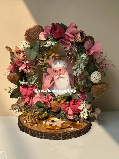 A sacred darbar honoring Guru Nanak Dev Ji, designed with rustic pink florals and natural elements on a wooden slice. The arrangement includes a golden 'Ek Onkar' symbol.