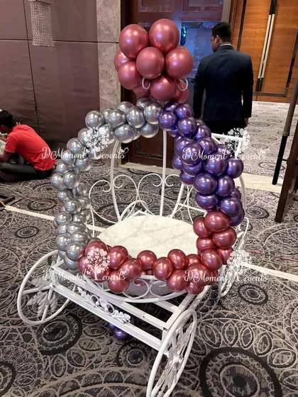A decorative white carriage adorned with a garland of metallic silver, purple, and maroon balloons. This prop adds a touch of fairytale elegance to any princess-themed event.