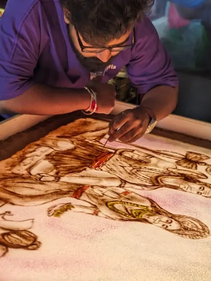 Working on a detailed sand art piece with multiple figures, using a fine tool to add precision.