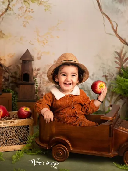 Driving through the apple orchard. This happy shot features a smiling toddler in a wooden car, holding an apple, perfectly capturing the fun of our rustic-themed sessions.