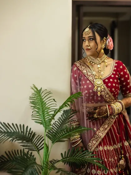 A candid shot of the bride in her stunning red lehenga. The makeup is soft and elegant, with a focus on creating a natural, radiant glow that looks beautiful in any light.