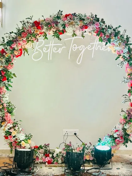 Elegance for a 'Roka' or engagement ceremony. This stunning circular arch is crafted entirely from fresh, multi-colored flowers, centered with a "Better Together" neon sign to create a beautiful focal point for the couple.