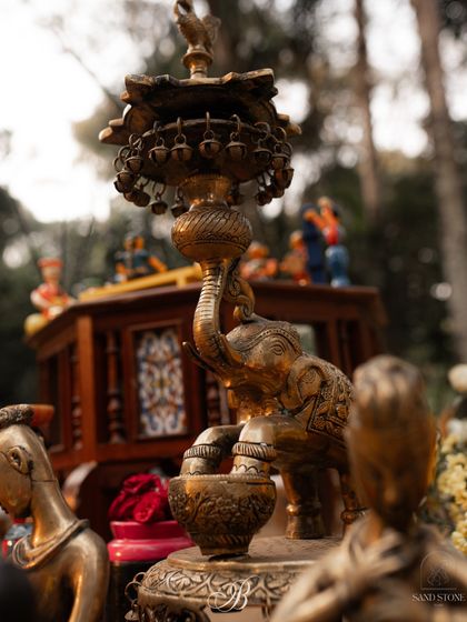 A stunning brass elephant lamp stands among other traditional artifacts. I love using antique brass pieces to add a sense of history, elegance, and warmth to the wedding decor.
