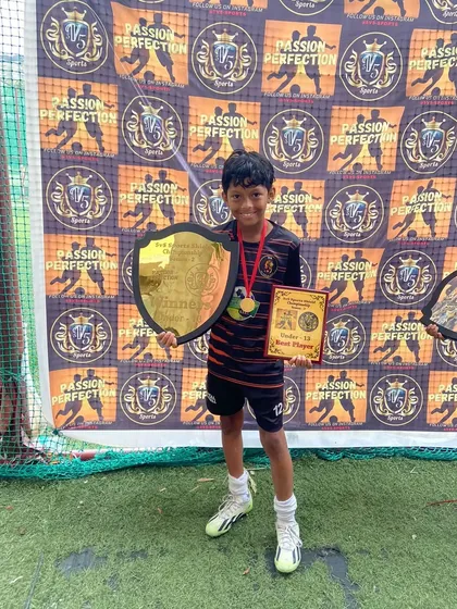 A proud champion from our U13 team holding his best player award and the winner's shield.