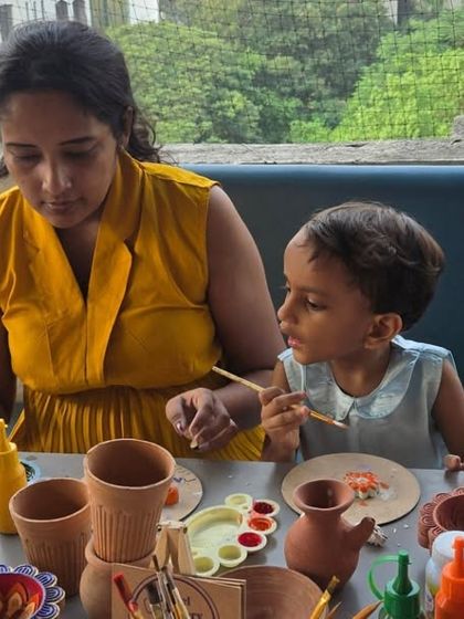 A beautiful moment of a mother and her young child painting together. The table is full of terracotta pots and colorful paints, ready for their artistic touch.
