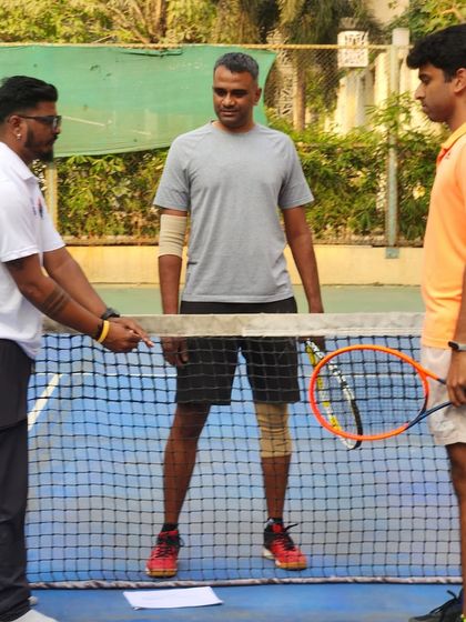 A coach provides instruction to a player at the net. Our tennis coaching focuses on personalized feedback to help players refine their technique and court strategy.