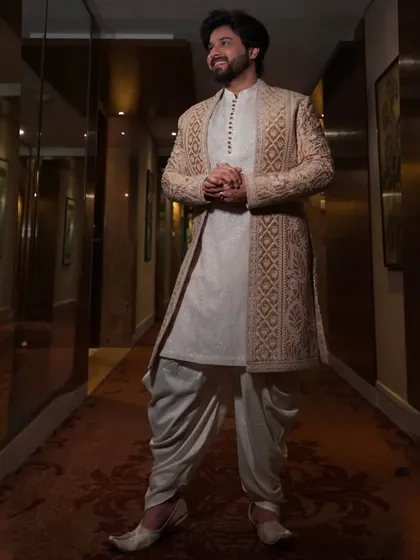 This beige open indowestern jacket features geometric embroidery and is paired with a dhoti-style salwar for a traditional yet stylish look.