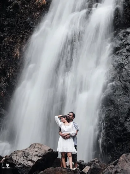 A full view of the couple embracing in front of a large waterfall. This shot showcases the scale and beauty of the natural location.