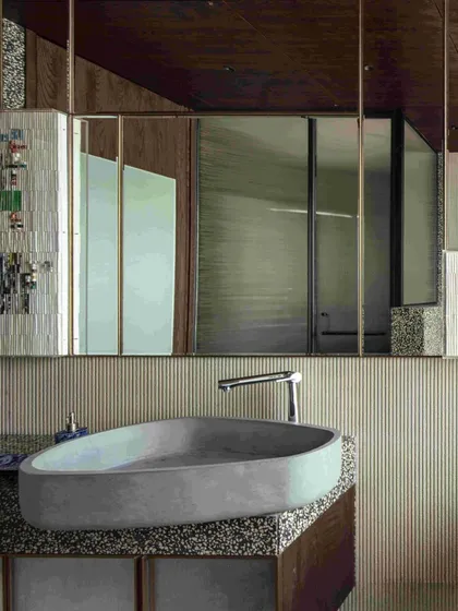 A close-up of the pebble-shaped concrete wash basin and fluted limestone wall paneling. The design plays with organic shapes and linear textures to create a serene and stylish sanctuary.