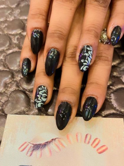 A dark and elegant design on almond-shaped nails. The glossy black polish is enhanced with accent nails featuring a delicate, light blue floral pattern.
