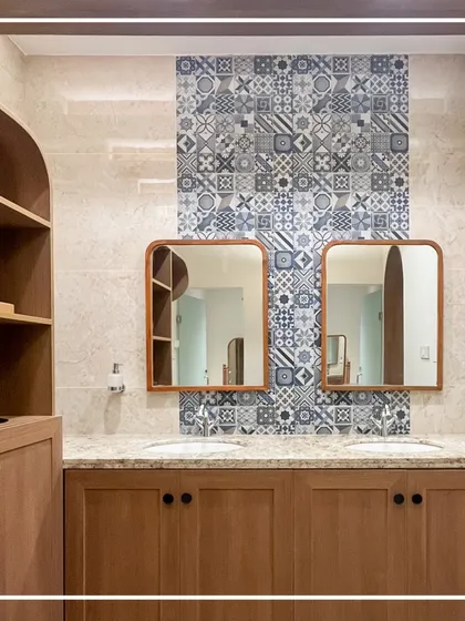 In the ladies' washroom, a feature wall of patterned blue tiles provides a vibrant contrast to the warm wood cabinetry and colonial gold stone countertops. The custom-framed mirrors with rounded corners soften the space, blending classic and contemporary design elements.