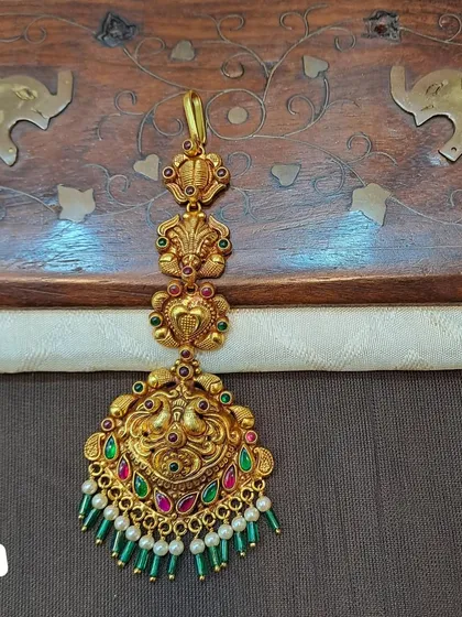 A beautiful peacock motif maang tikka made from 92.5 silver with gold plating. The green and pearl bead drops add a touch of elegance to this traditional piece.