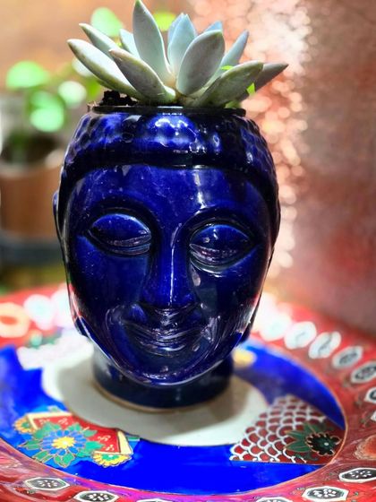 A ceramic Buddha-head planter painted a brilliant blue. Our pottery painting sessions allow you to add your personal touch to pre-made ceramic items, creating unique decor for your home.