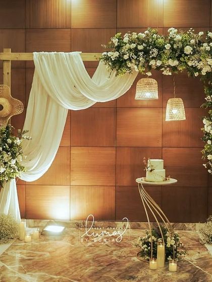 A rustic yet elegant engagement stage with a wooden arch draped in white fabric and adorned with white florals. The setting is illuminated by candles, creating a warm and romantic glow.