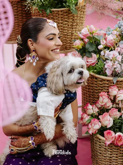 The most important guest of honor! A heartwarming shot of the bride holding her beautifully dressed-up dog amidst the vibrant decor of her Mehendi ceremony.