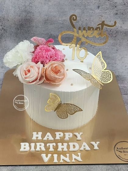 A sweet 16 cake that is both elegant and charming. The white cake is decorated with fresh flowers and delicate golden butterflies.