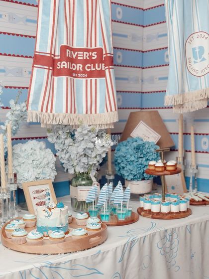 The dessert table at the sailor party, featuring a nautical-themed cake, cupcakes, and custom-printed towels hanging in the background.