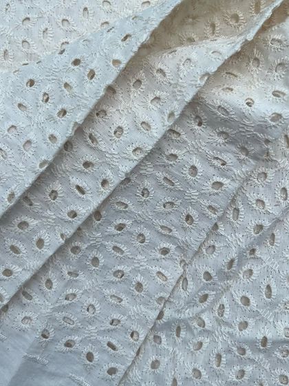 A classic white cutwork cotton with a delicate eyelet pattern. This fabric is perfect for creating sophisticated and breathable summer outfits.