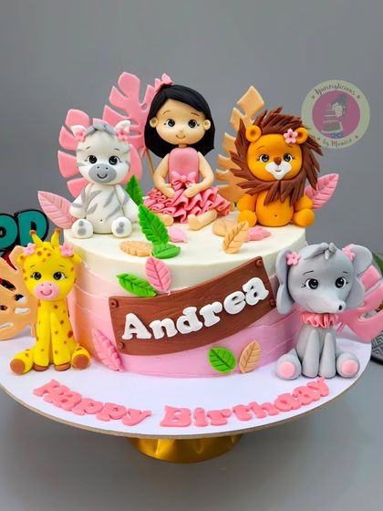 A pink jungle-themed cake for little Andrea, featuring a custom girl figurine surrounded by cute, friendly safari animals.