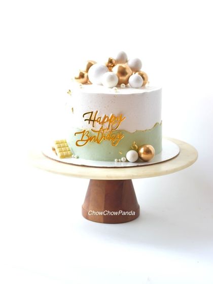 A simple yet elegant birthday cake with a light green and white design. This Chocolate Raspberry cake is topped with white and gold spheres for a clean, modern finish.