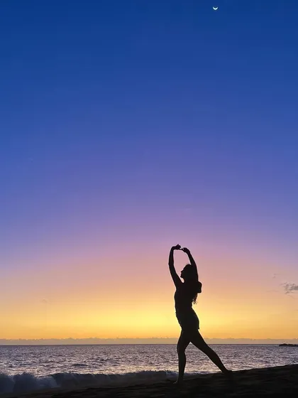A silhouette of a dance pose against a stunning sunset on a black sand beach in Reunion Island. This artistic shot emphasizes form and grace in a breathtaking natural setting.