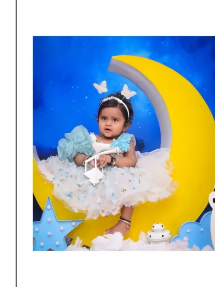 This little girl looks serene and thoughtful, sitting on a big yellow moon surrounded by fluffy clouds. The dreamy, celestial theme is a popular choice for baby photoshoots.