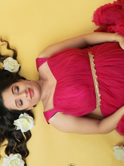 A beautiful top-down shot of a mother-to-be lying on a yellow background. Her vibrant red gown and hair adorned with white roses create a striking and artistic image.