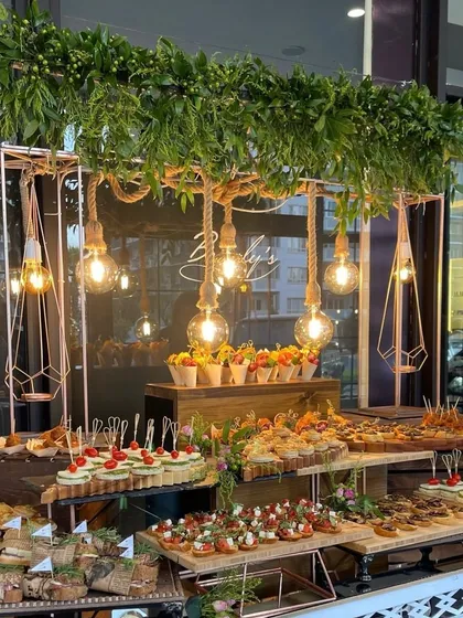 We can design catering stations that match your event's theme. This rustic-chic food stall features industrial-style lighting and greenery, beautifully presenting a variety of small bites.