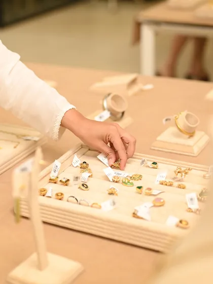 The tactile experience of choosing jewelry. A client carefully examines a tray of rings, feeling the weight and seeing the details of each handcrafted piece.