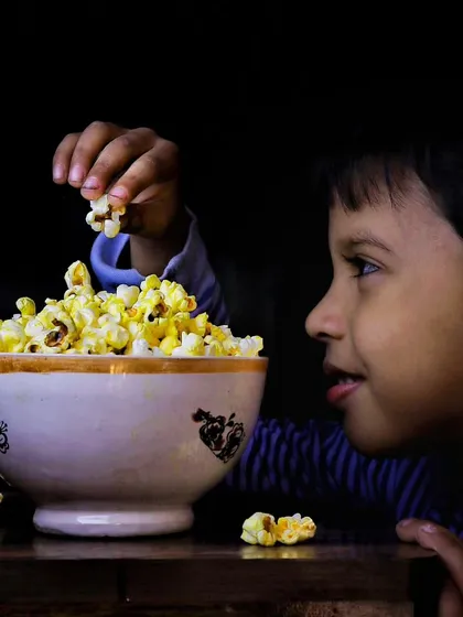 A candid portrait of my son enjoying a bowl of popcorn, captured with dramatic lighting to highlight his expression. These are the *mera bachcha* moments that I love to freeze in time.