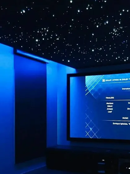 The ambiance of a theater is paramount. Here, a fiber optic starfield ceiling is paired with deep blue ambient lighting to create a captivating environment. The on-screen Dolby Atmos menu indicates the presence of an advanced, object-based surround sound system for a three-dimensional audio experience.