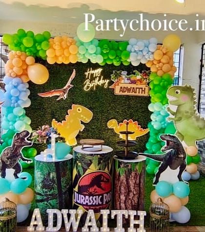 A prehistoric adventure with our dinosaur theme. This outdoor setup includes a faux grass wall, a variety of dinosaur cutouts including a T-Rex and Triceratops, and a bright green, yellow, and blue balloon arch.