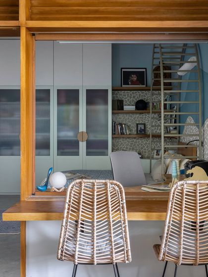 A creative workspace featuring wicker chairs and a view into an adjoining room. The design uses a pass-through window to maintain a sense of connection while defining a separate area for work or study.