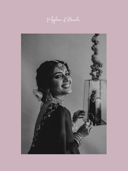 A joyful, candid moment captured in black and white. The bride's smile is the centerpiece, beautifully framed by her elegant updo and statement jewelry.
