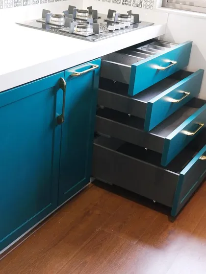 This kitchen, designed for a prominent social media influencer, showcases a classic shaker-style design with a rich teal PU finish. The image highlights the deep, organized drawers that are a hallmark of my commitment to functional storage.