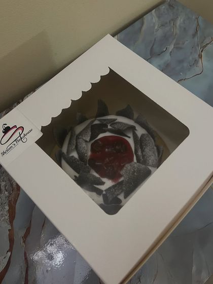 This is a classic Black Forest cake, ready to be delivered. You can see the layers of moist chocolate sponge, whipped cream, and cherries, all packaged beautifully for your celebration.