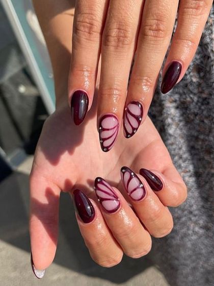 An elegant and artistic design featuring deep maroon nails and accent nails with hand-painted butterfly wings on a sheer base.