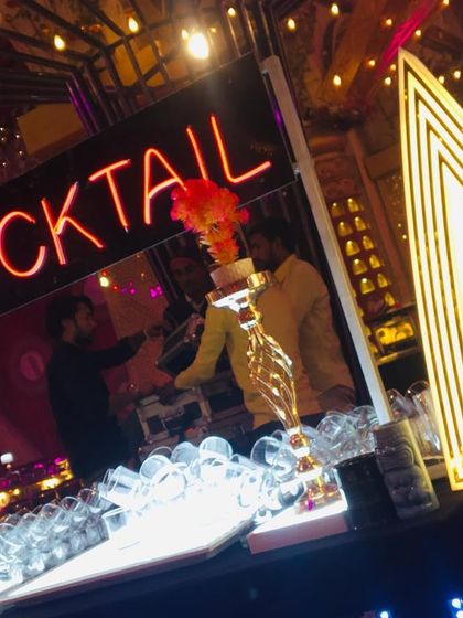 A 'Cocktail' neon sign glows above the bar as our team serves guests, capturing the lively energy of the event.