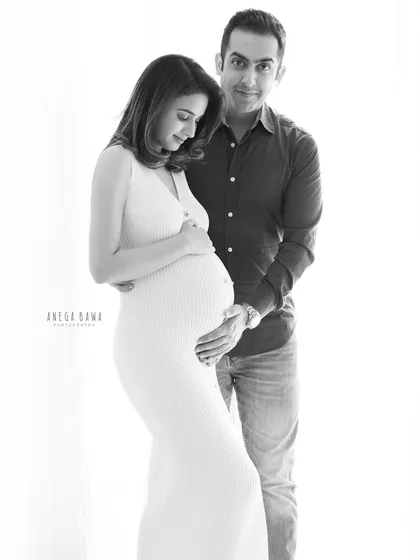 A quiet, elegant portrait of a couple in black and white. The focus is on their gentle embrace and the beautiful shape of the baby bump.