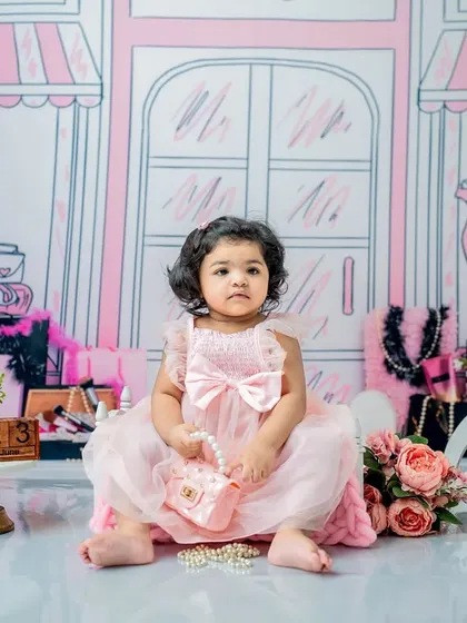 A classic seated pose for a first birthday. This little girl in a soft pink dress holds her purse, looking like a true little lady in her Barbie-themed photoshoot.
