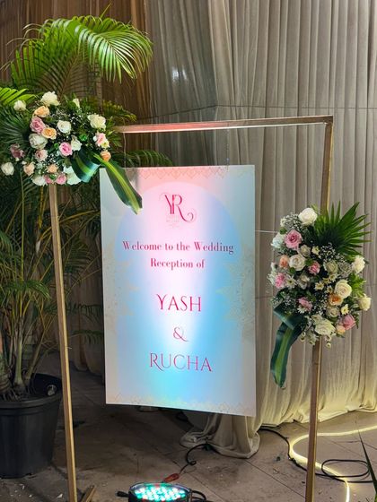 A minimalist and modern welcome sign for the reception, on a simple gold frame and adorned with two elegant floral bouquets.