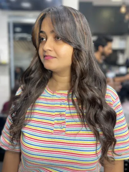 A playful and modern look with curtain bangs and light brown highlights on wavy hair.
