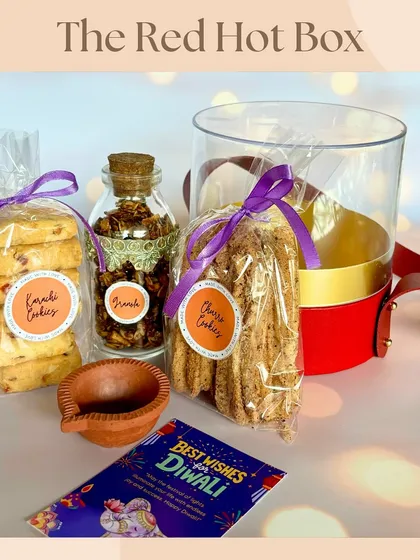 The 'Red Hot Box' Diwali hamper, a stylish cylindrical box containing Karachi cookies, cheese cookies, a granola jar, and a diya. A modern and tasty festive offering.